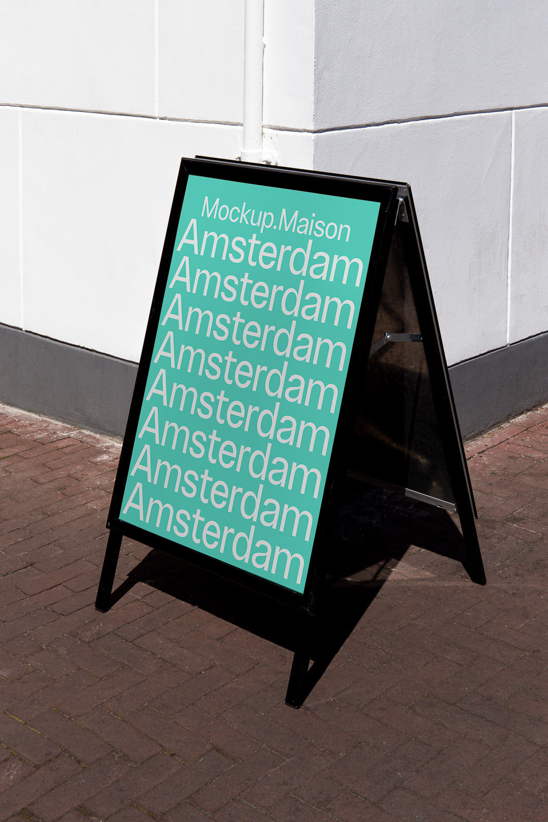 PSD mockup of an A-frame sign on a street corner featuring the repeated text "Amsterdam" in white on a teal background, leaning against a white wall.