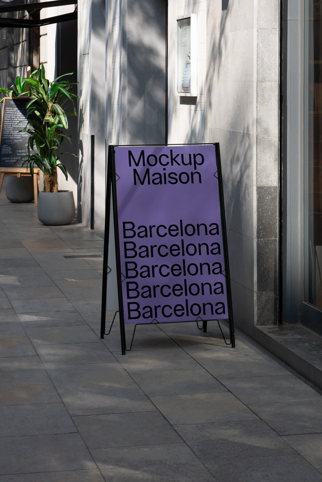 PSD mockup of a purple A-frame sign with "Mockup Maison" and "Barcelona" text, positioned on a city sidewalk beside a building and potted plant.