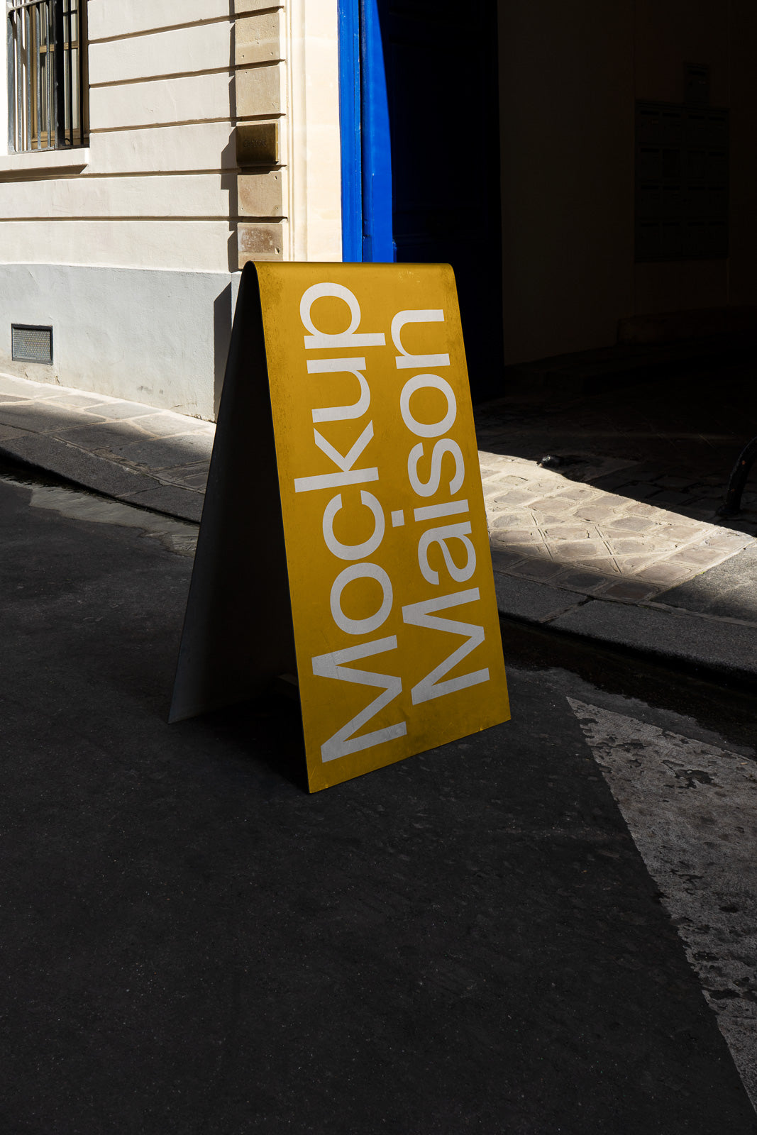 PSD mockup of a yellow sandwich board on a city street with the text "Mockup Maison" in large white letters against a building wall.