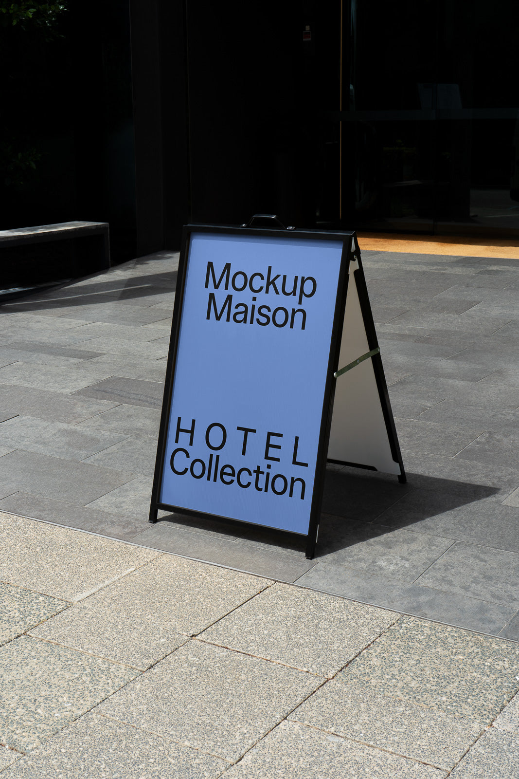 PSD mockup of a freestanding pavement sign featuring the text "Mockup Maison HOTEL Collection" on a blue background, set outdoors on a stone walkway.