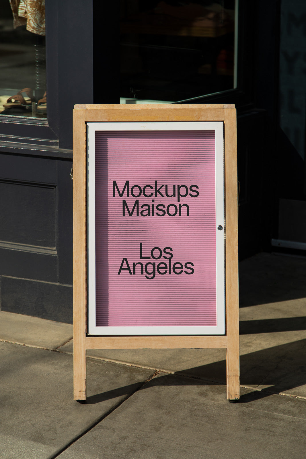 PSD mockup of a wooden A-frame sandwich board displaying "Mockups Maison Los Angeles" on a light pink background, placed on a sidewalk.