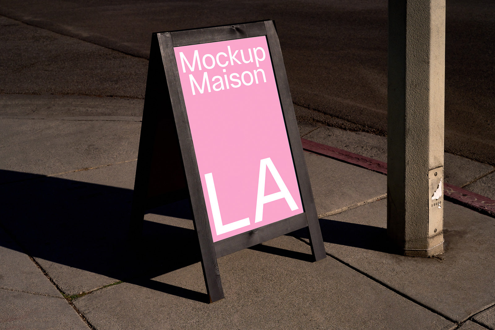 PSD mockup of a sidewalk sign with a pink background and white text reading "Mockup Maison LA," standing on concrete pavement next to a pole.