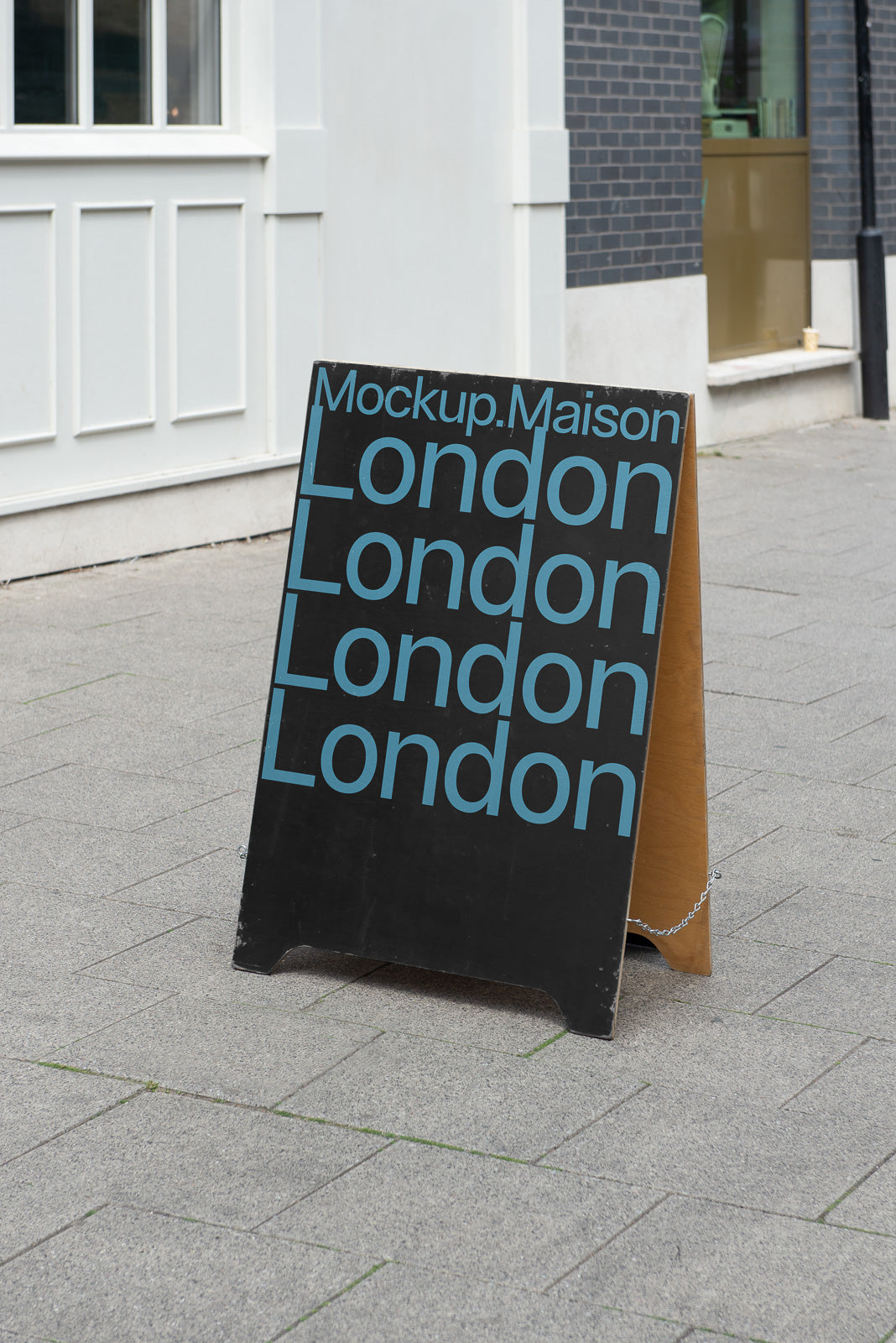 PSD mockup of an A-frame sidewalk sign featuring the word "London" repeated in blue text on a black background, placed on a city street.