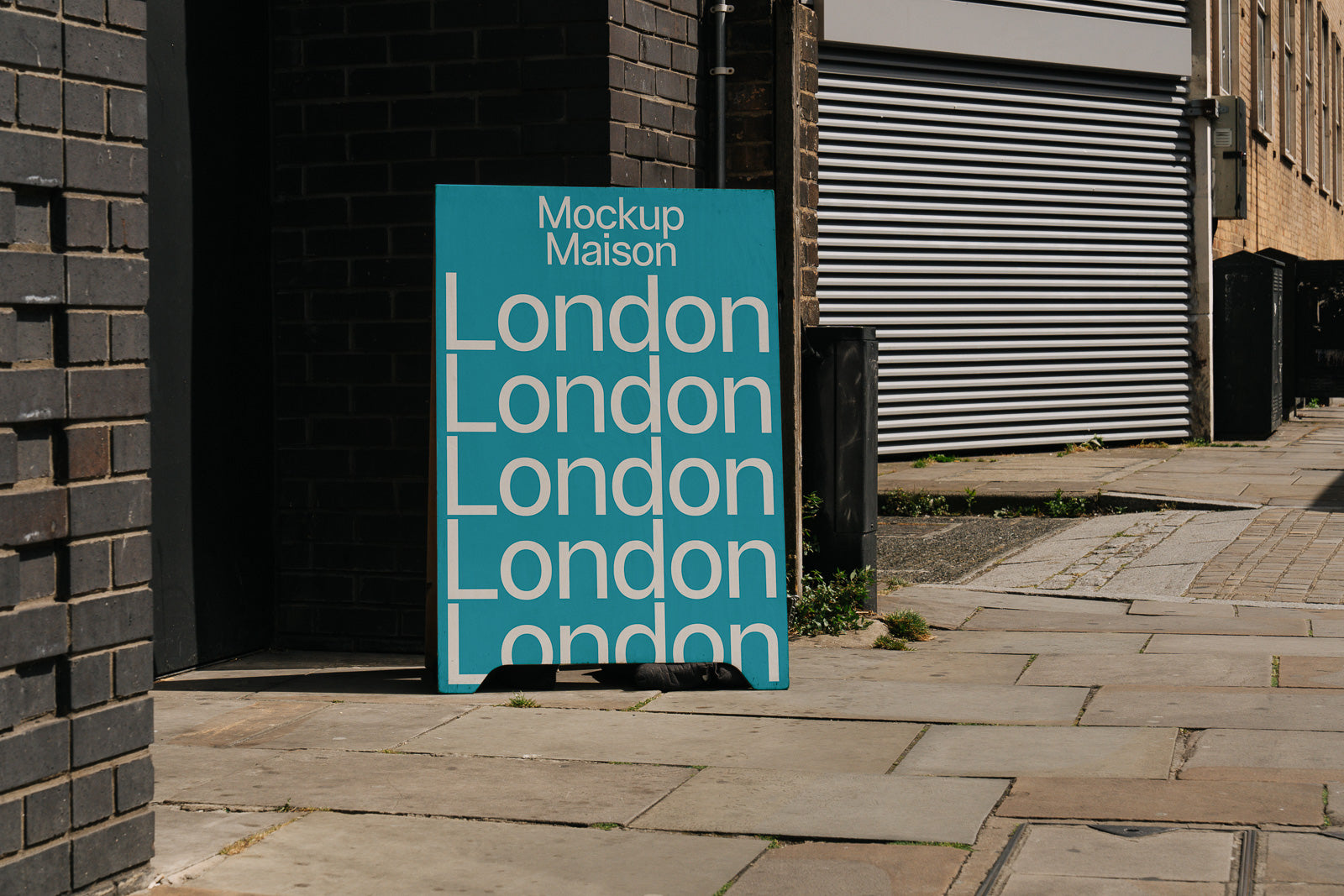 PSD mockup of a turquoise poster leaning against a brick wall, displaying the word "London" multiple times in white text on an urban street.