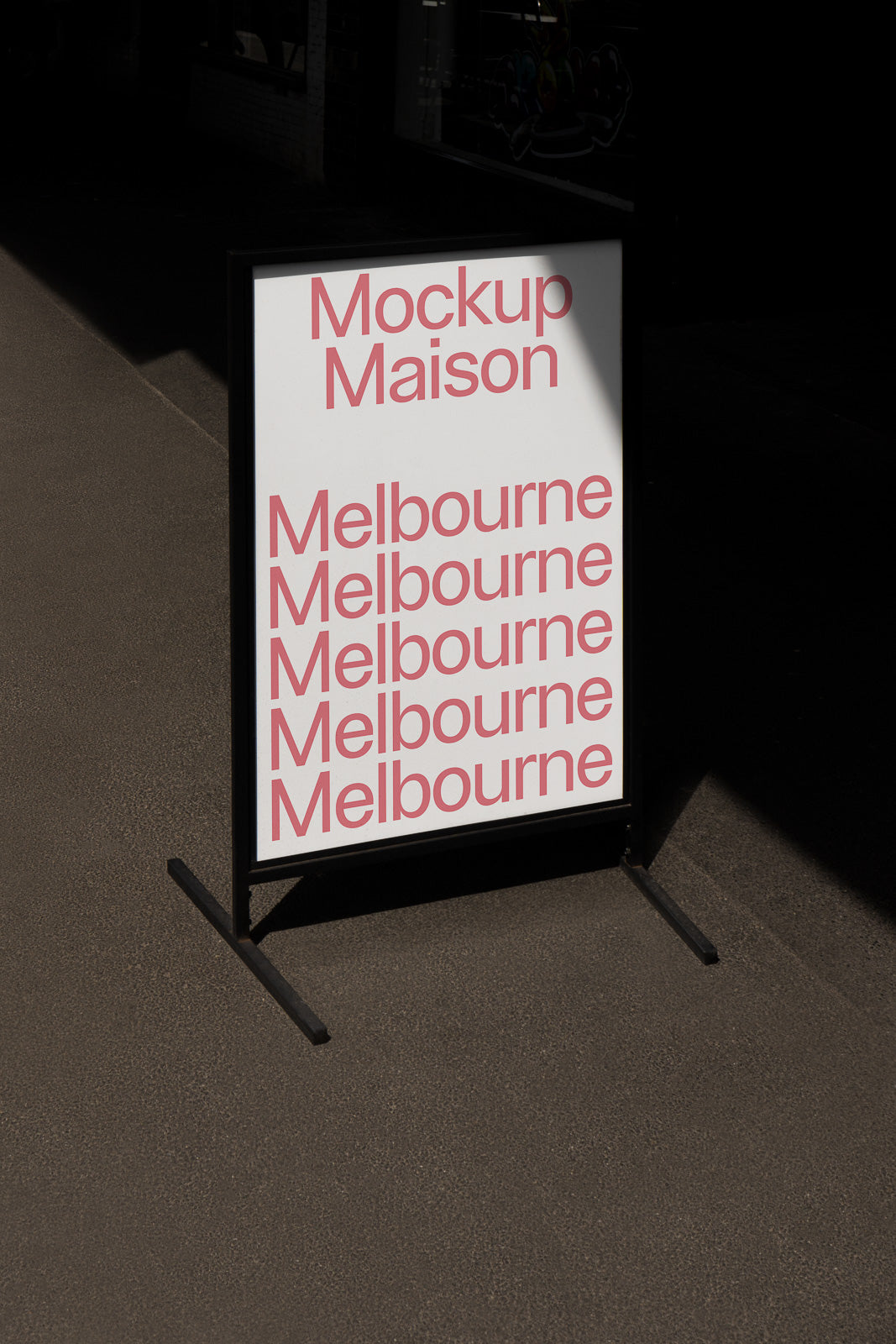 PSD mockup of a sidewalk sign featuring red typography with the repeated word "Melbourne" under the title "Mockup Maison" on a shadowed urban street.