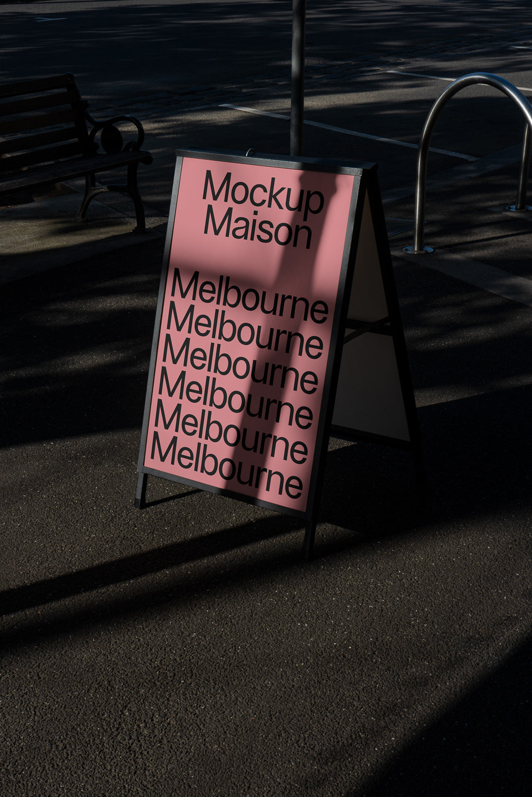 PSD mockup of an A-frame sign on a sidewalk, featuring "Mockup Maison" and "Melbourne" repeated multiple times in black on a pink background.