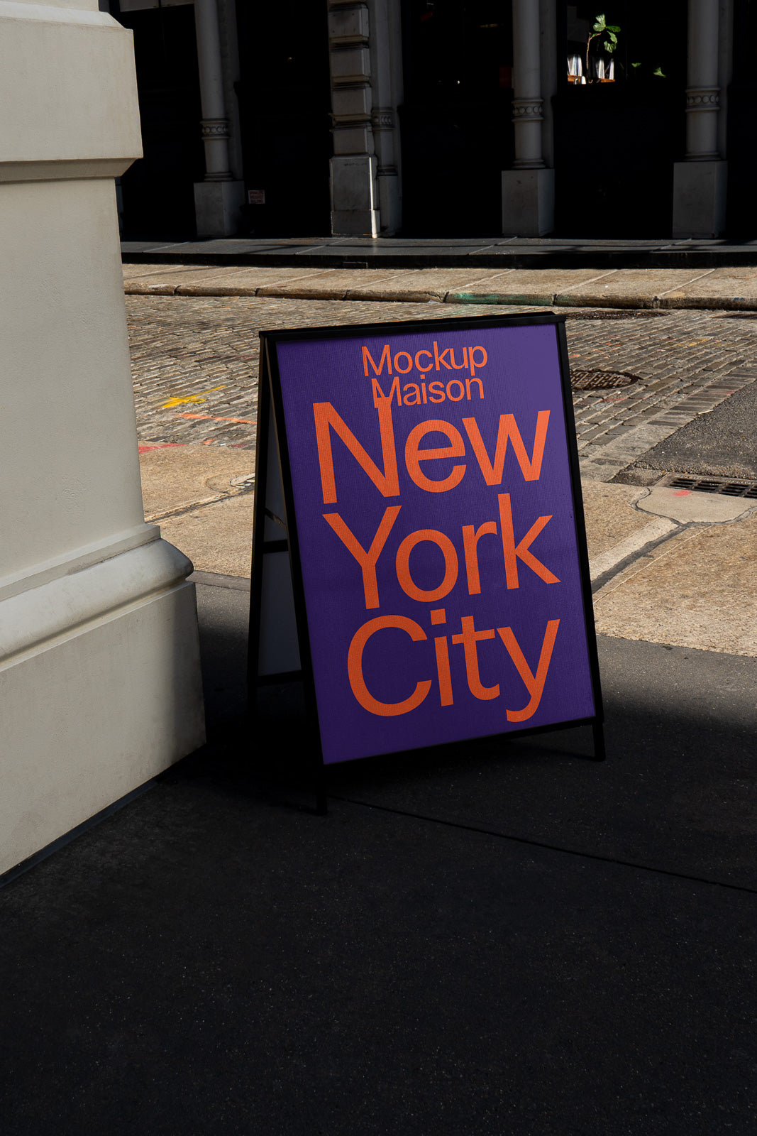 PSD mockup of a black A-frame sidewalk sign with vivid orange "New York City" text on a purple background, placed on an urban street corner.