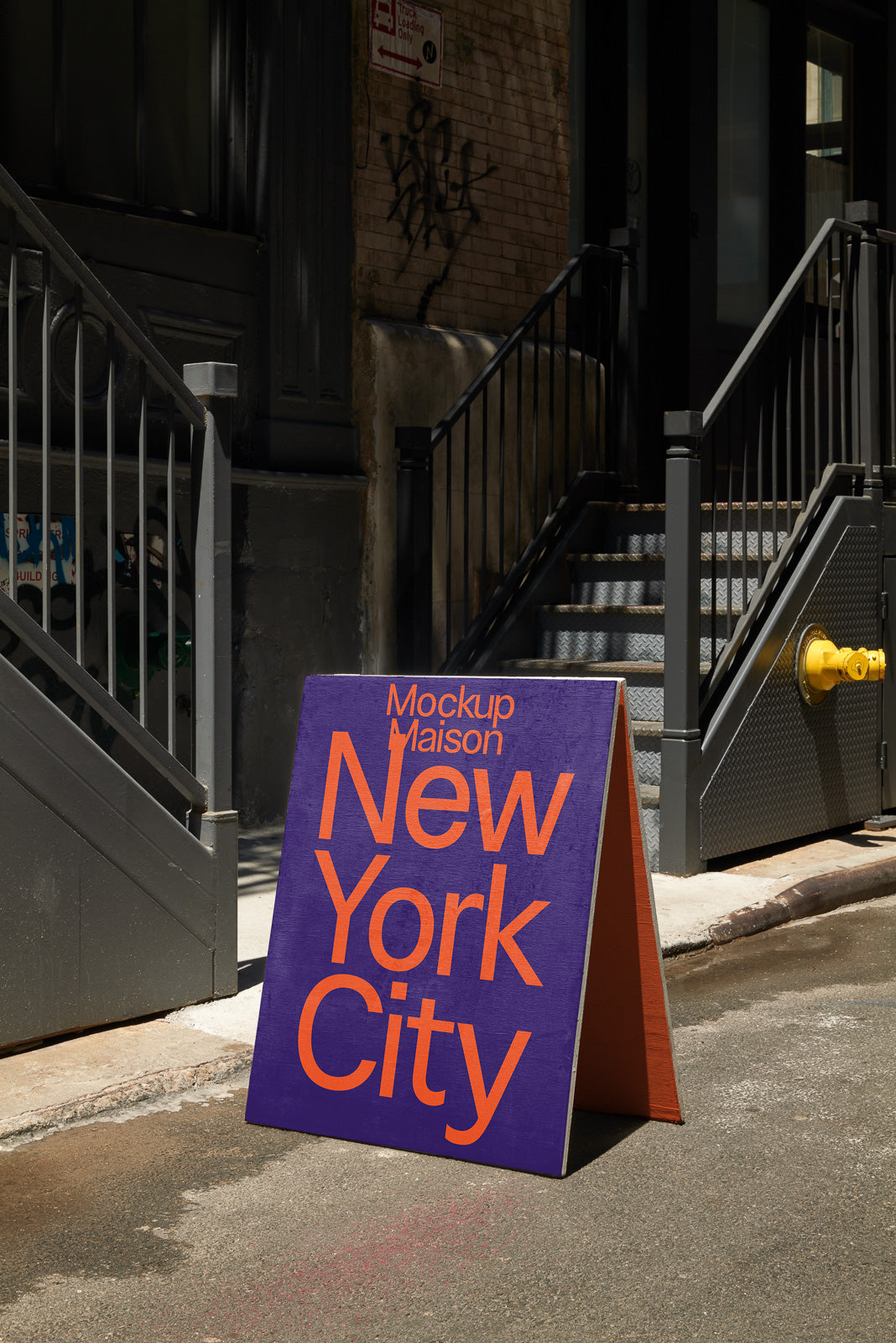 PSD mockup of a freestanding sandwich board sign with "Mockup Maison New York City" in bold orange text on a purple background, placed on an urban street.