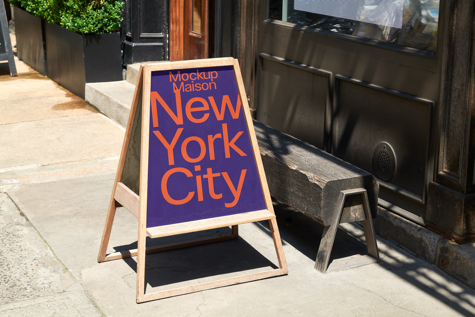 PSD mockup of a wooden sandwich board displaying "New York City" in bold orange letters on a purple background placed on a sidewalk.