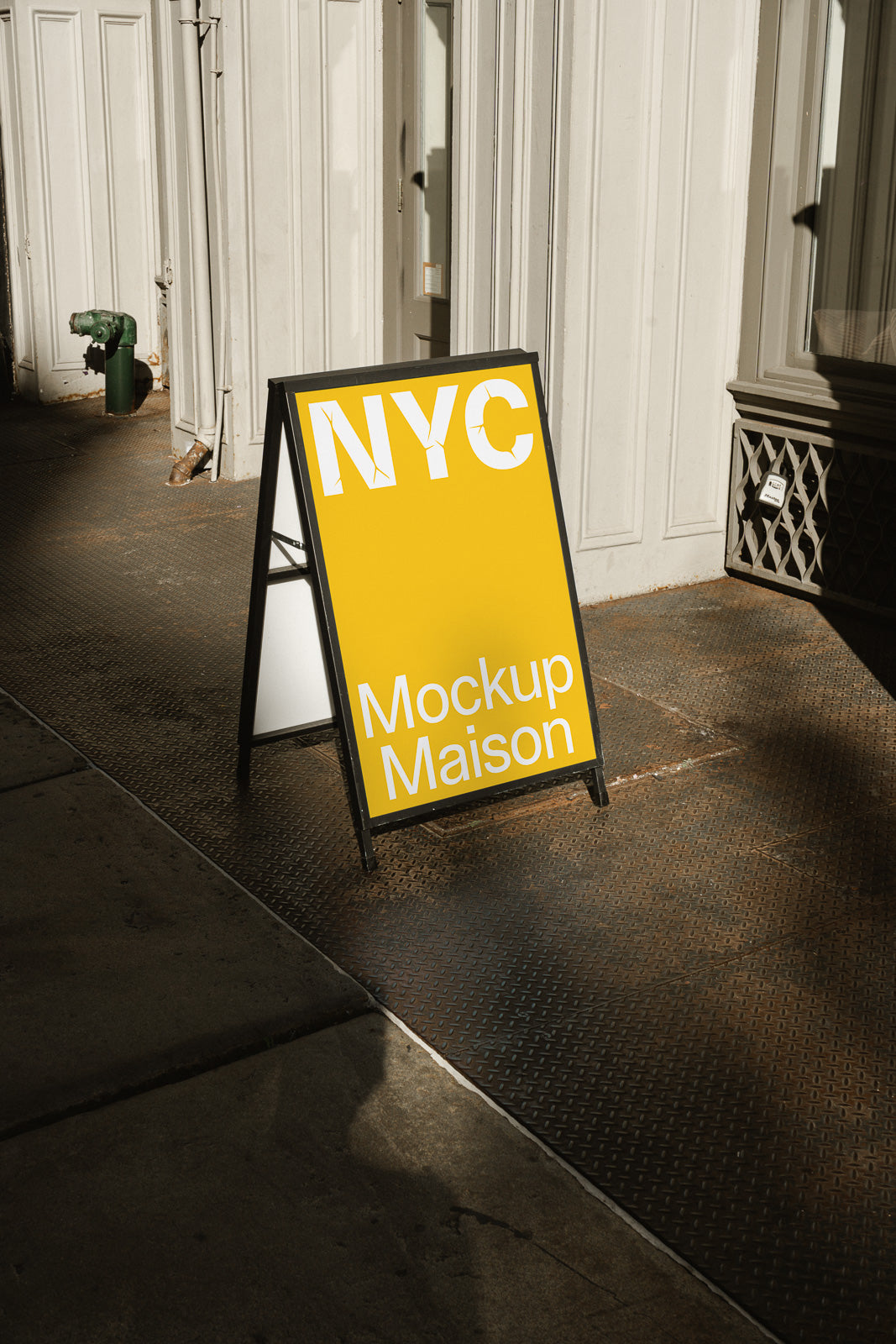 PSD mockup of an A-frame sidewalk sign with "NYC" and "Mockup Maison" on a yellow background, placed on an urban street.