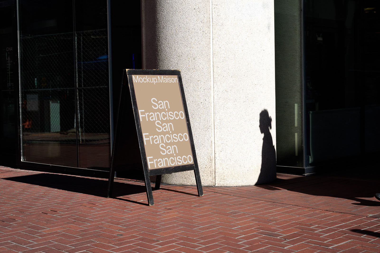 PSD mockup of a freestanding signboard outside a building, displaying "San Francisco" three times on a beige background, with sunlight casting a shadow.