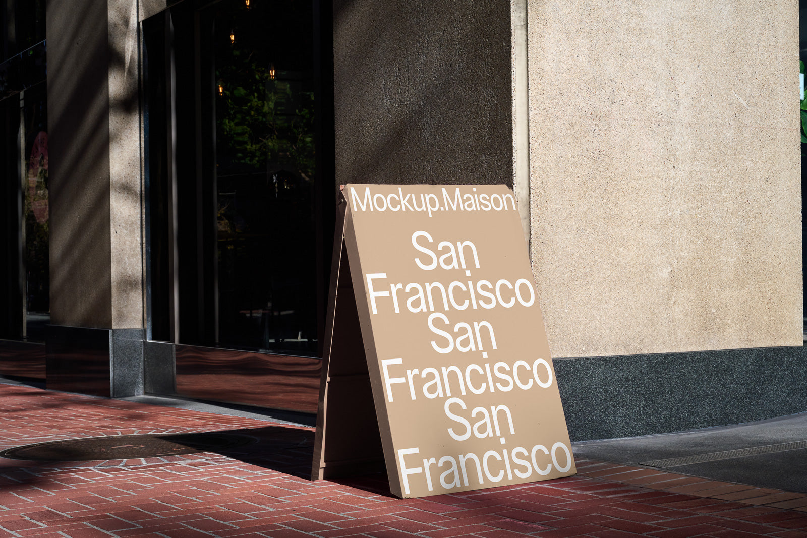 PSD mockup of a sandwich board displaying the text "Mockup.Maison San Francisco" against a building with brick sidewalk in the sunlight.