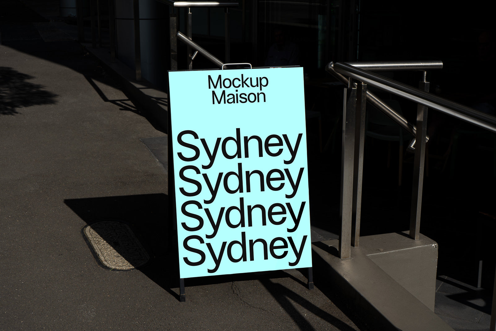 PSD mockup of a sidewalk sign displaying the word "Sydney" four times in black text on a light blue background, with sunlight and shadows.