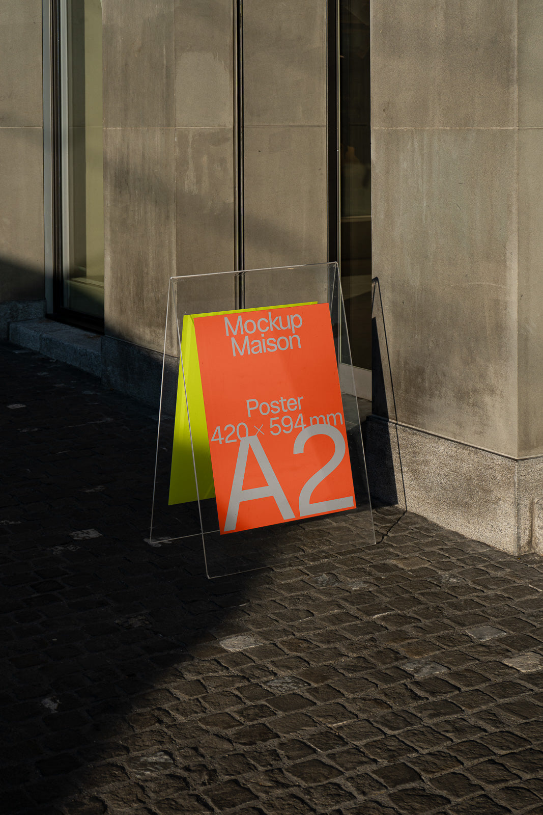 PSD mockup of a transparent stand displaying an A2 poster with orange and yellow design in an outdoor urban setting.