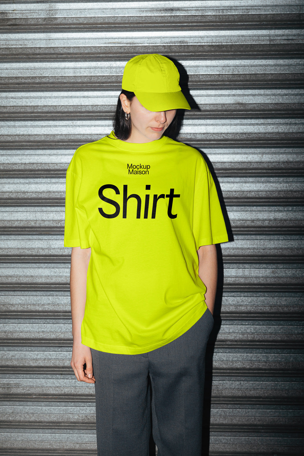 PSD mockup of a person wearing a bright yellow T-shirt and cap against a corrugated metal background. The shirt features bold text design.