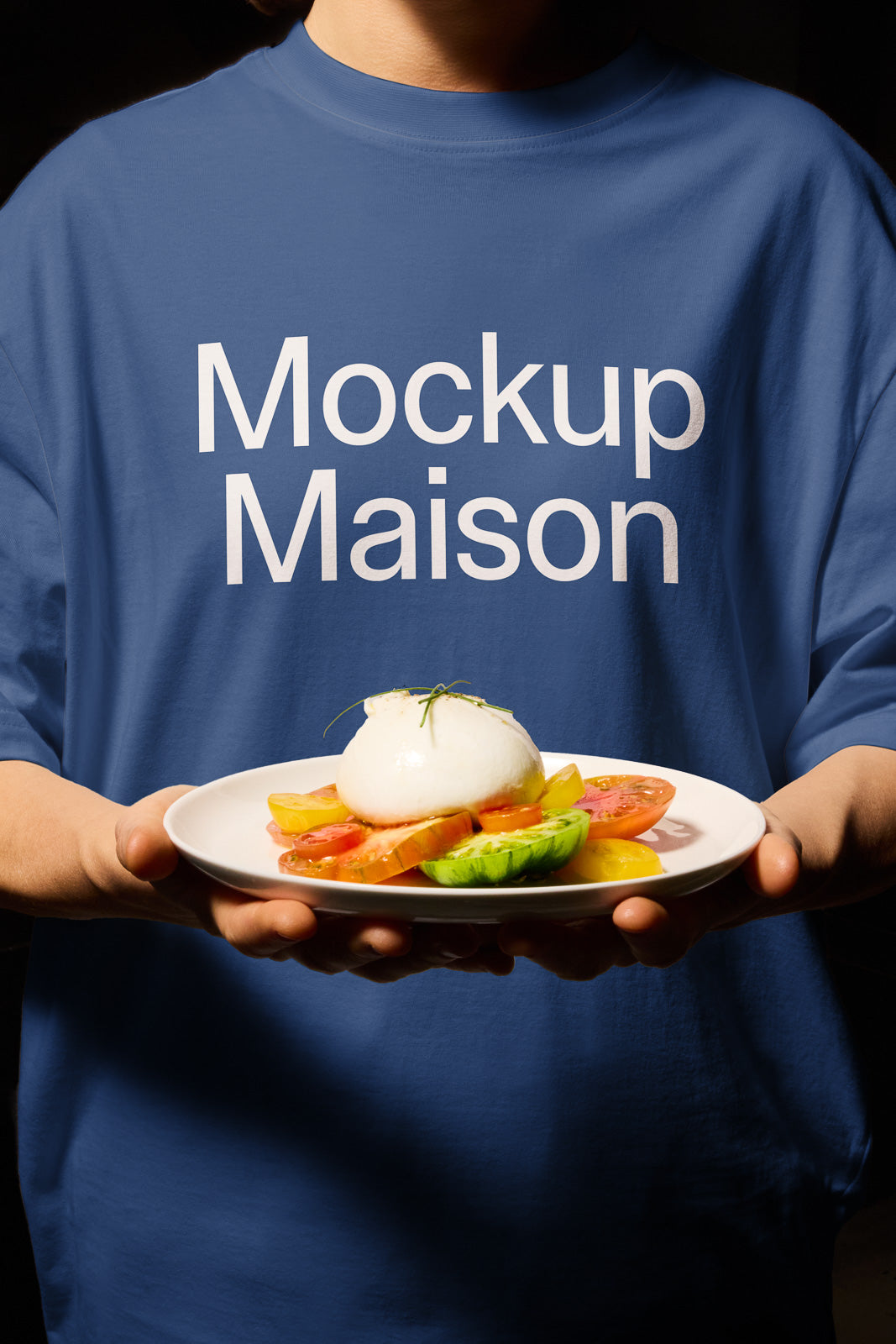 PSD mockup of a person in a blue shirt labeled "Mockup Maison" holding a plate with a ball of mozzarella on sliced tomatoes and cucumbers.