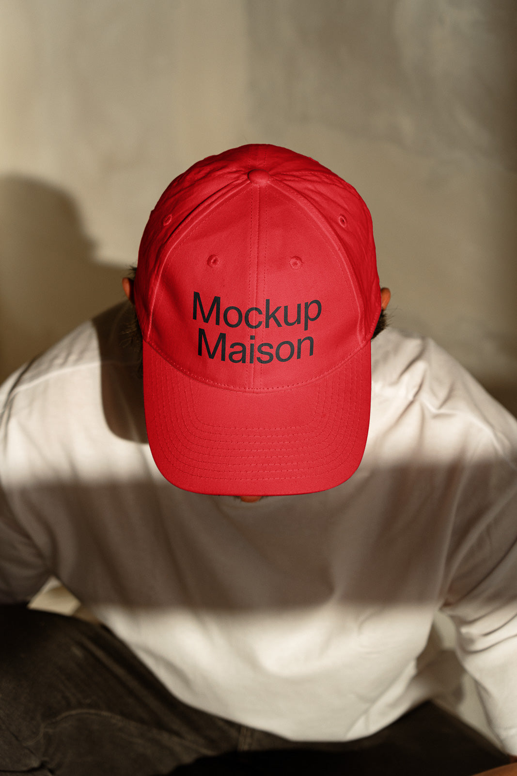 PSD mockup of a person wearing a red cap with the text "Mockup Maison" while seated, highlighting the cap design against a neutral background.