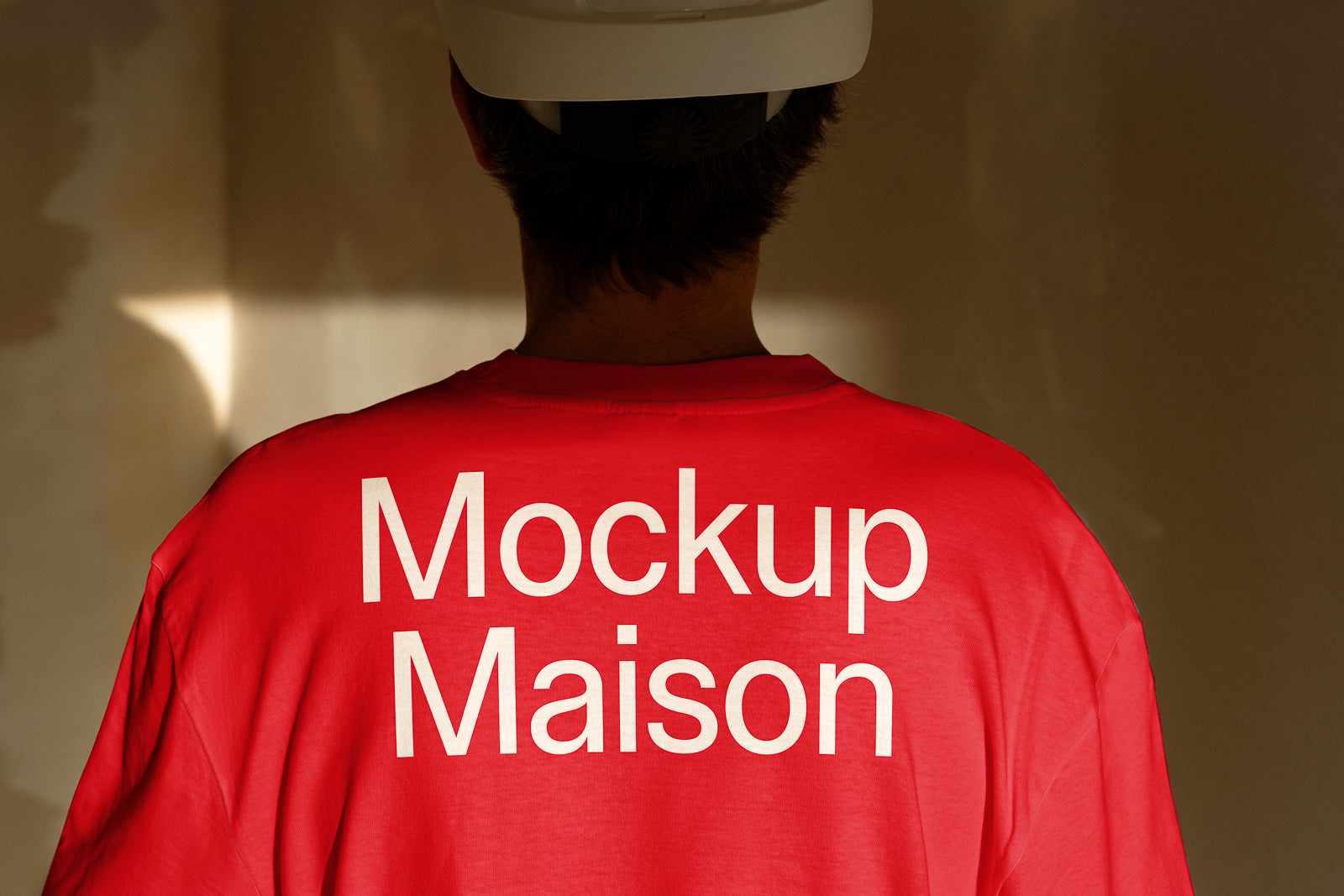 PSD mockup of a person wearing a red shirt with "Mockup Maison" text on the back, standing against a softly lit background.