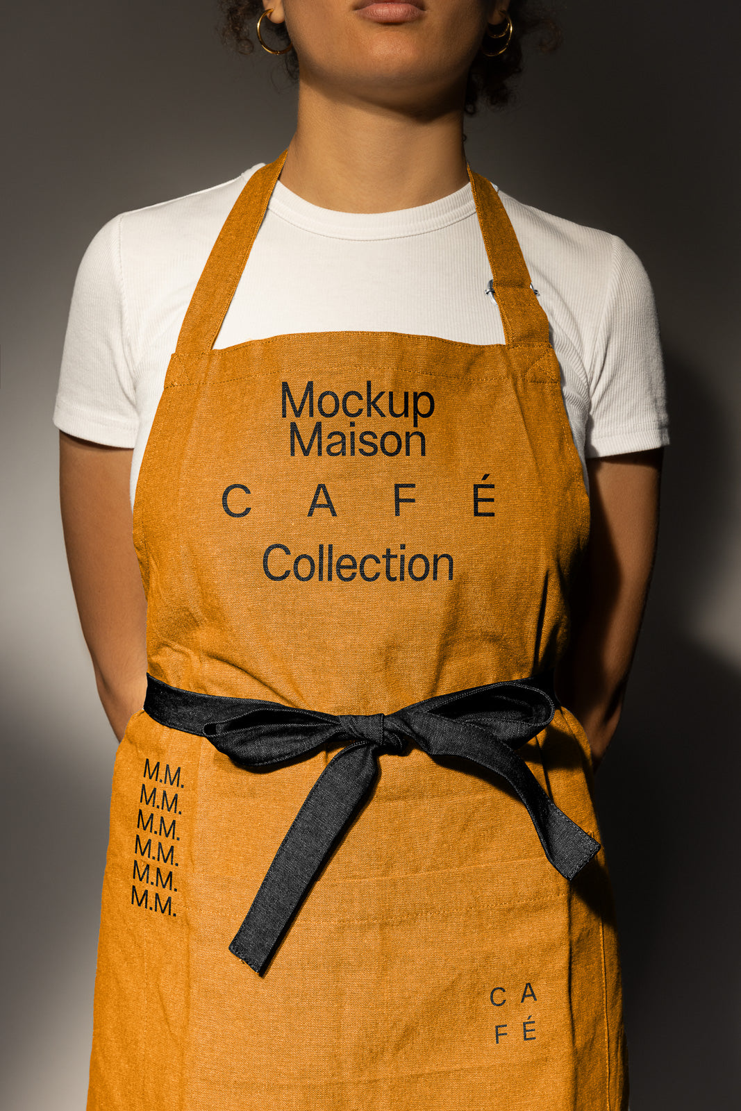 PSD mockup of an apron with "Mockup Maison Café Collection" text, worn over a white shirt, featuring a black ribbon and minimal design for branding.