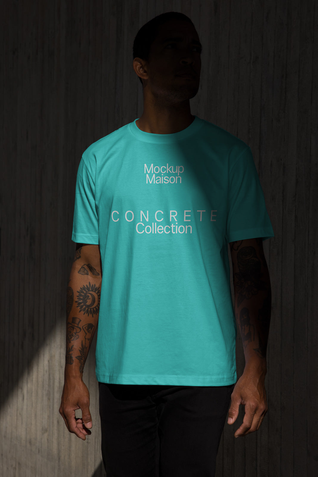 PSD mockup of a person wearing a teal T-shirt with "Mockup Maison" and "Concrete Collection" text, standing against a dark textured background.