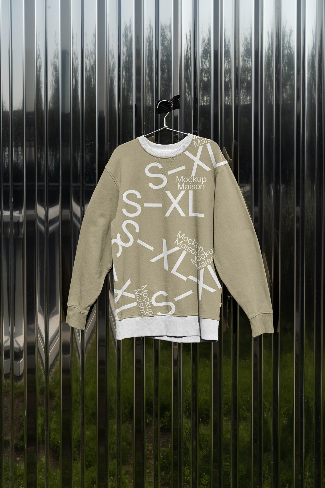 PSD mockup of a beige sweatshirt with white text design, including "S-XL" and "Mockup Maison," hanging on a metallic, reflective surface.