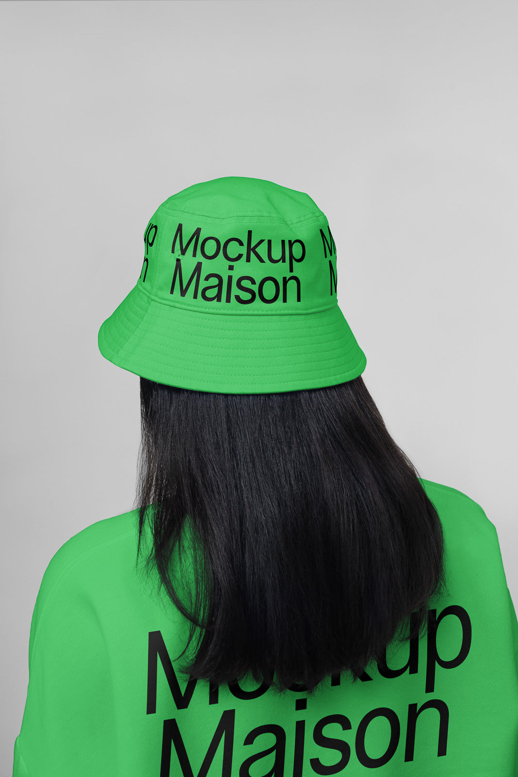 PSD mockup of a person wearing a green bucket hat and matching shirt, both featuring the text "Mockup Maison" in black, viewed from the back.