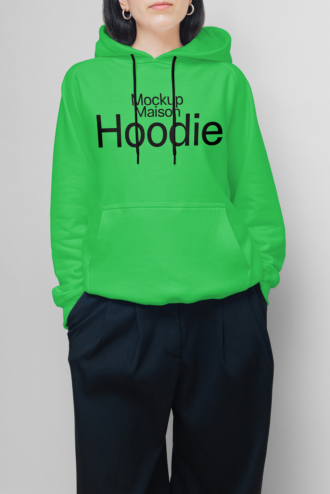 PSD mockup of person wearing a bright green hoodie with black text "Mockup Maison Hoodie" over dark pants against a gray background.