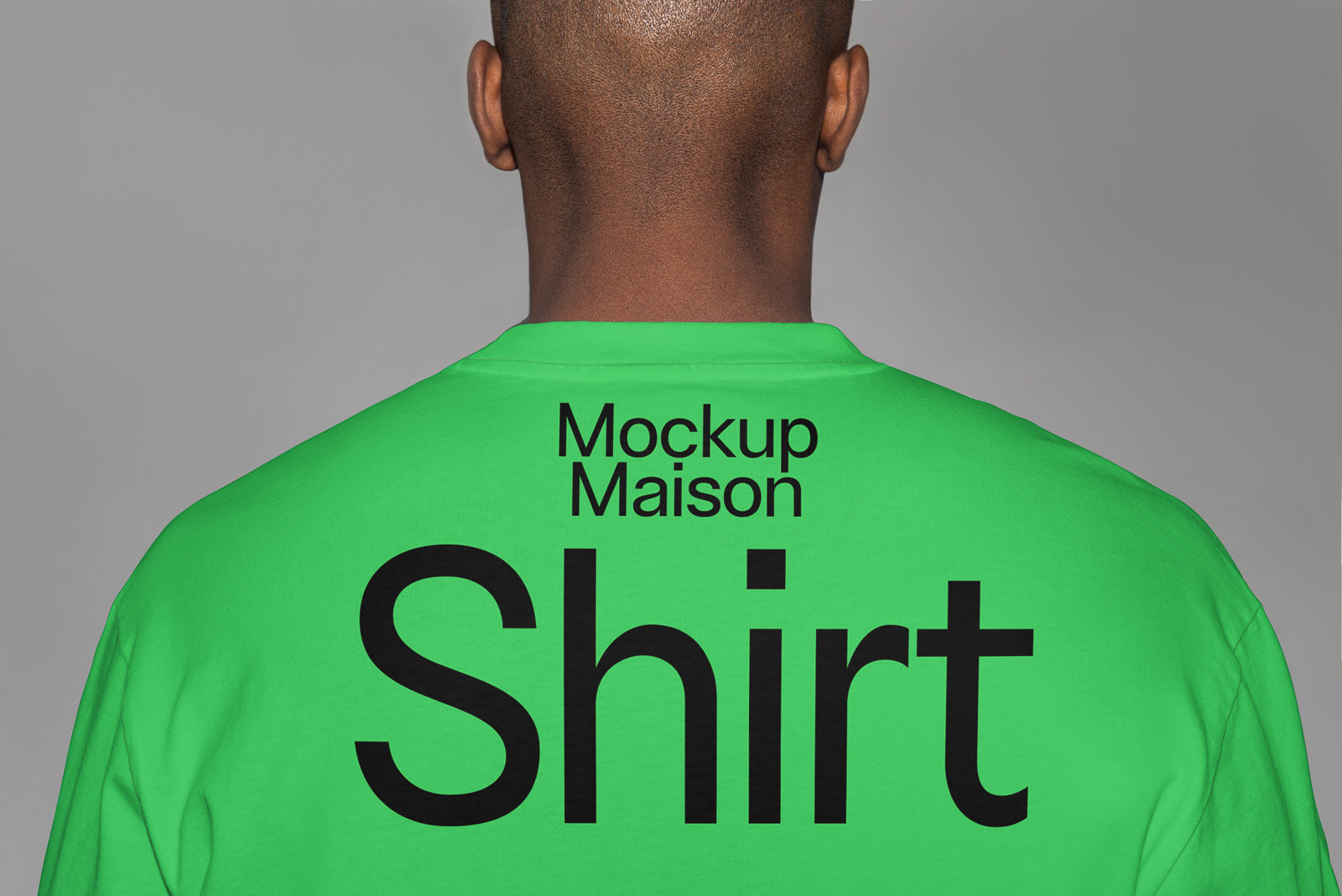 PSD mockup of a person wearing a green shirt with large black text reading "Shirt" and smaller text "Mockup Maison" on the back.