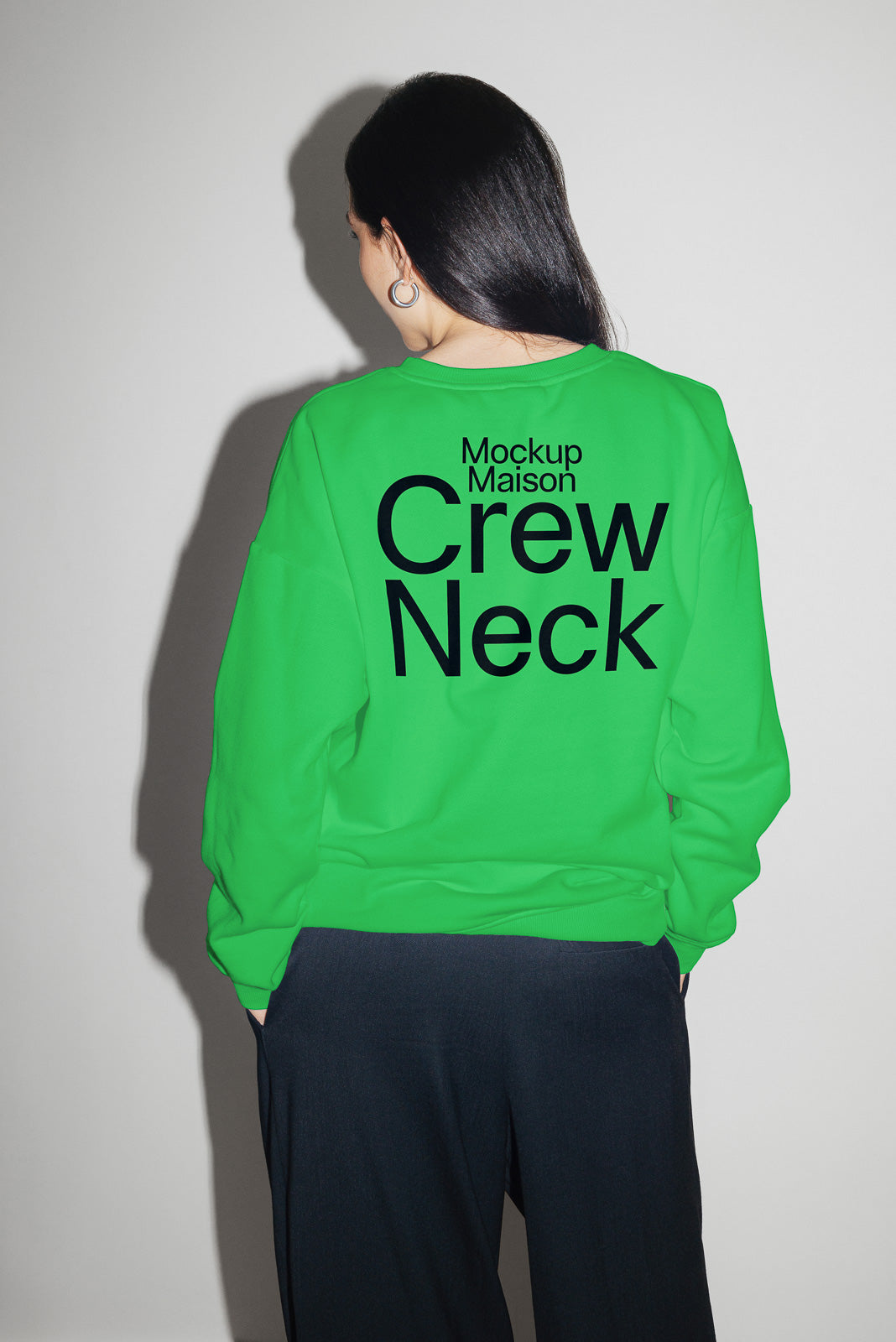 PSD mockup of a person wearing a vibrant green crew neck sweatshirt with bold black text reading "Mockup Maison Crew Neck" across the back, viewed from behind.