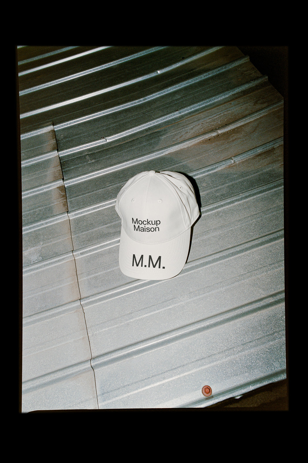PSD mockup of a white baseball cap with "Mockup Maison" and "M.M." text placed on a corrugated metal surface.