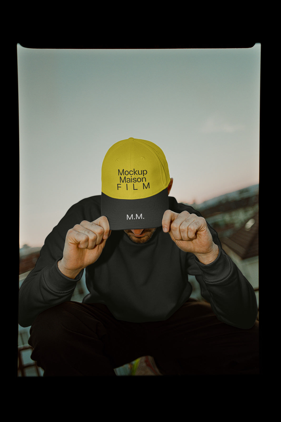 PSD mockup of a person wearing a black and yellow cap with text "Mockup Maison FILM" and "M.M." against a blurred cityscape background.