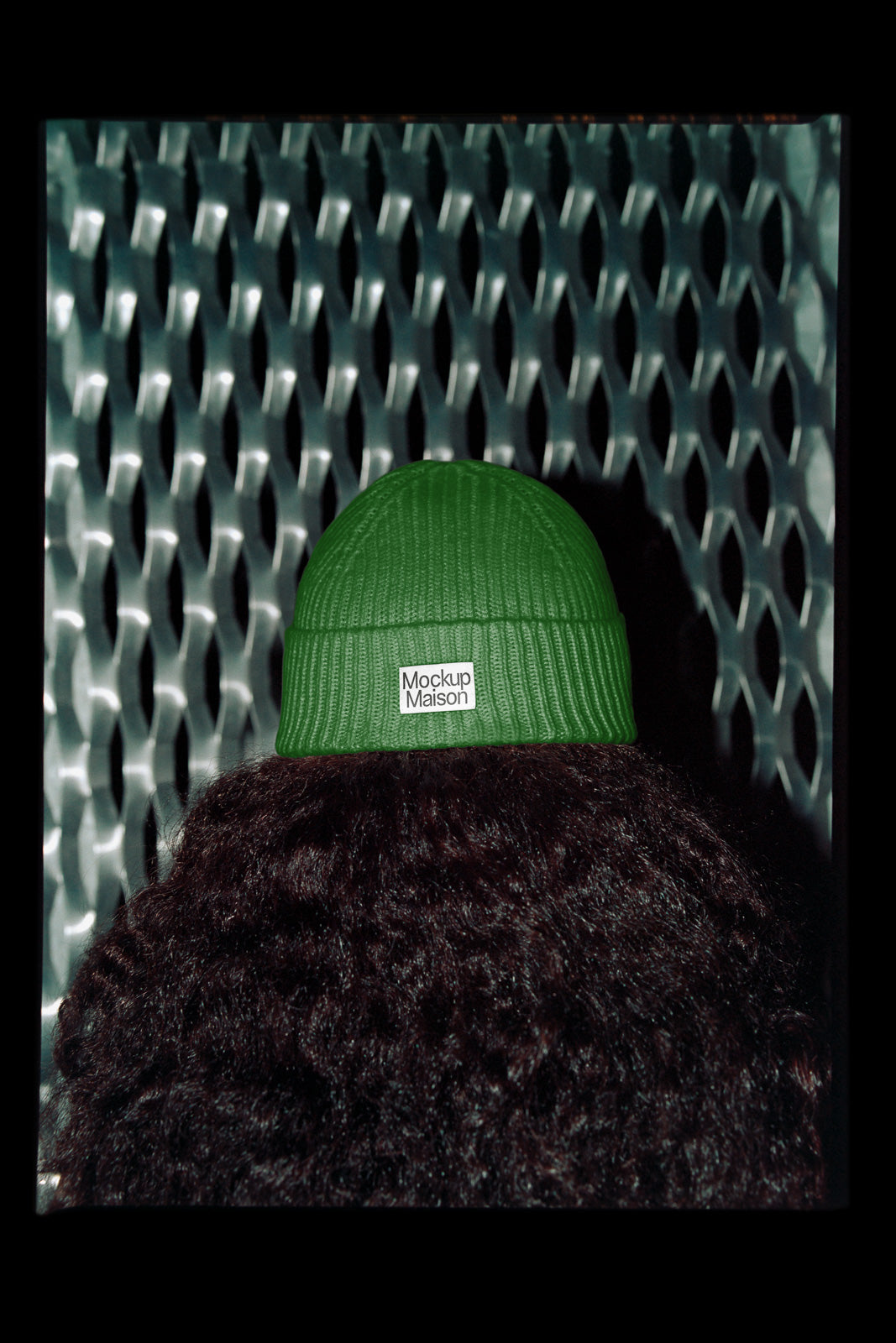 PSD mockup of a green knit beanie with a "Mockup Maison" label, worn by a person with curly hair, against a textured metal background.