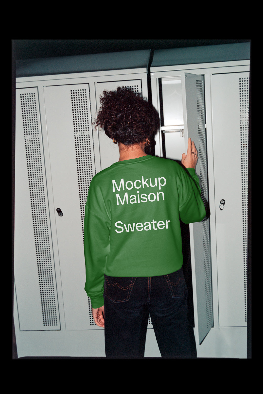 PSD mockup of a person wearing a green sweater with "Mockup Maison Sweater" text, standing in front of white lockers.