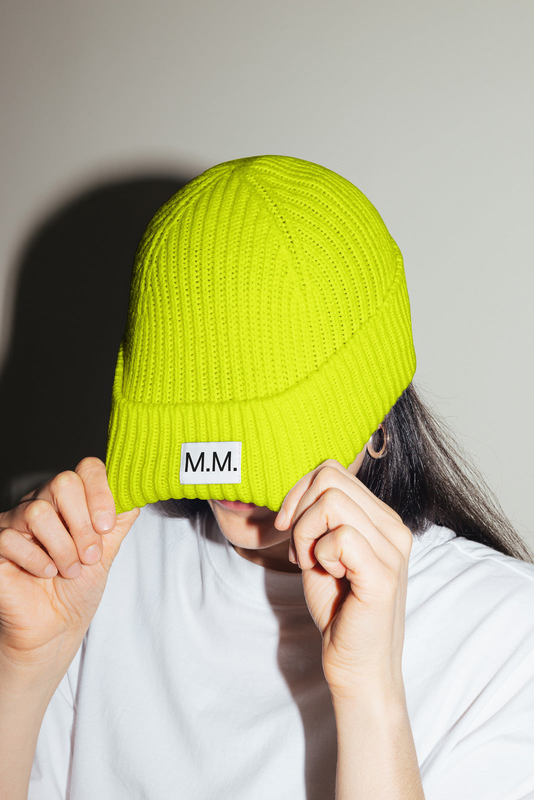 PSD mockup of a person wearing a bright yellow knit beanie with "M.M." label covering their face, dressed in a white shirt.