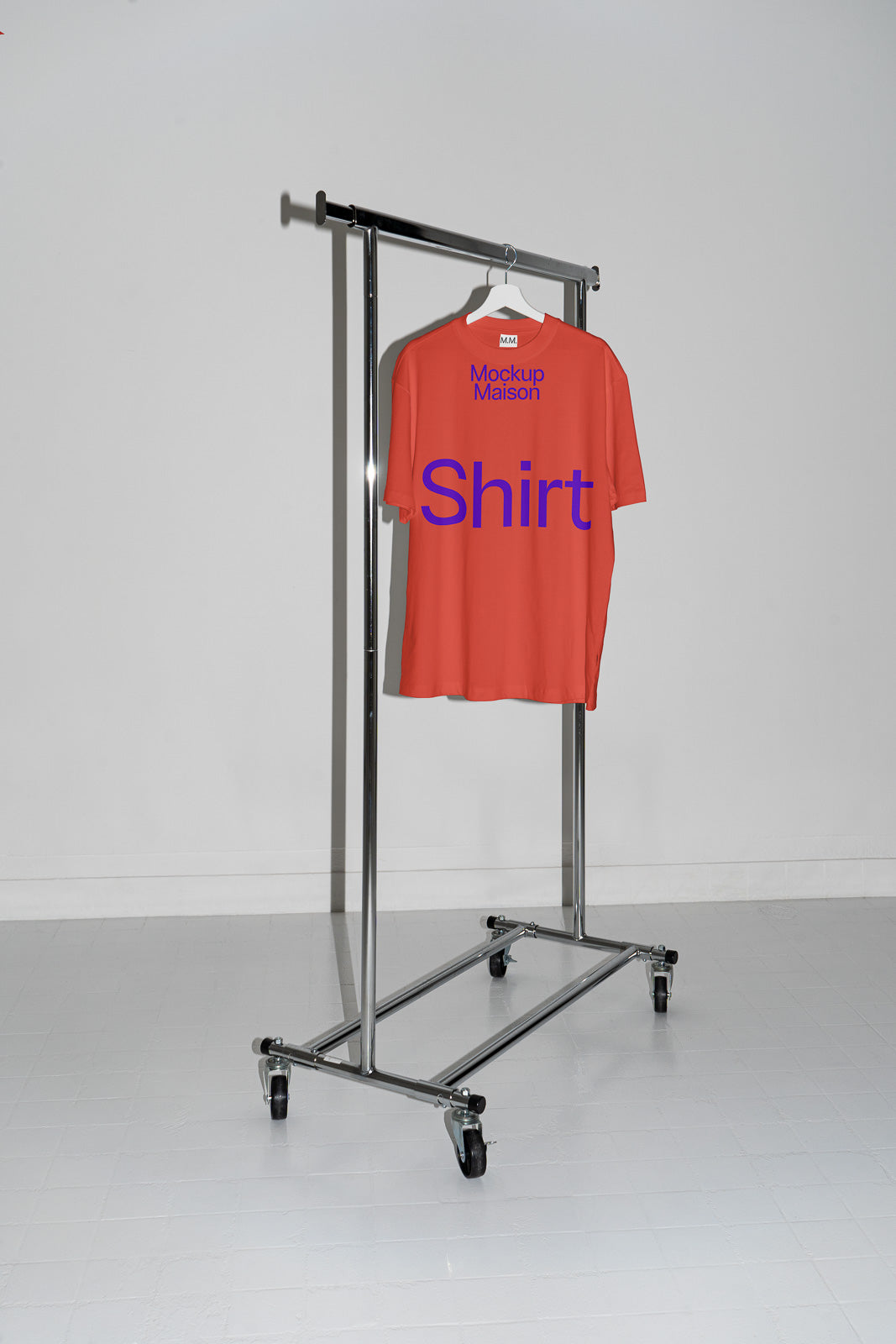 PSD mockup of a red T-shirt hanging on a metal clothing rack in a minimalist white room. The shirt features blue text and is displayed from the back.