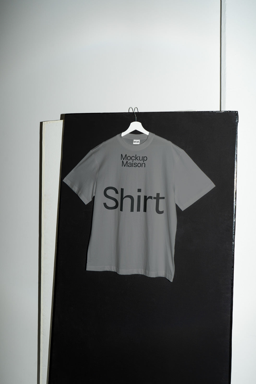 PSD mockup of a gray t-shirt on a hanger against a black and white background, featuring the text "Mockup Maison Shirt" printed on the front.