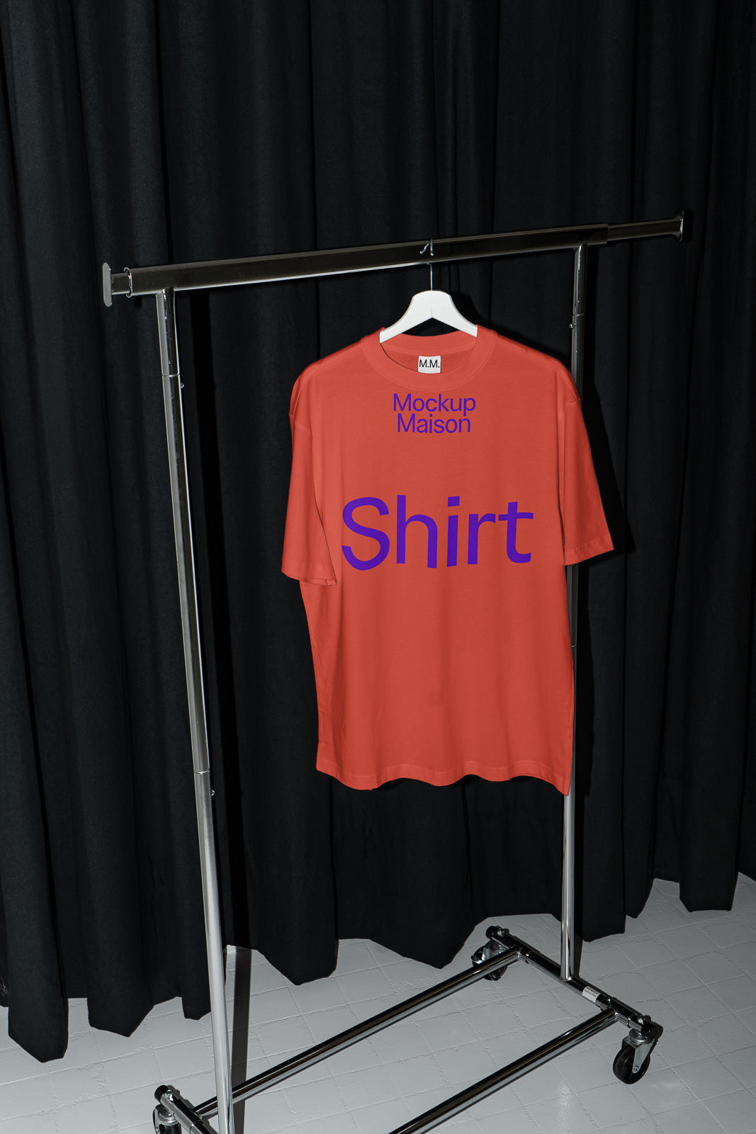 PSD mockup of a red T-shirt on a hanger with "Mockup Maison" and "Shirt" text, displayed against black curtains on a metal garment rack.