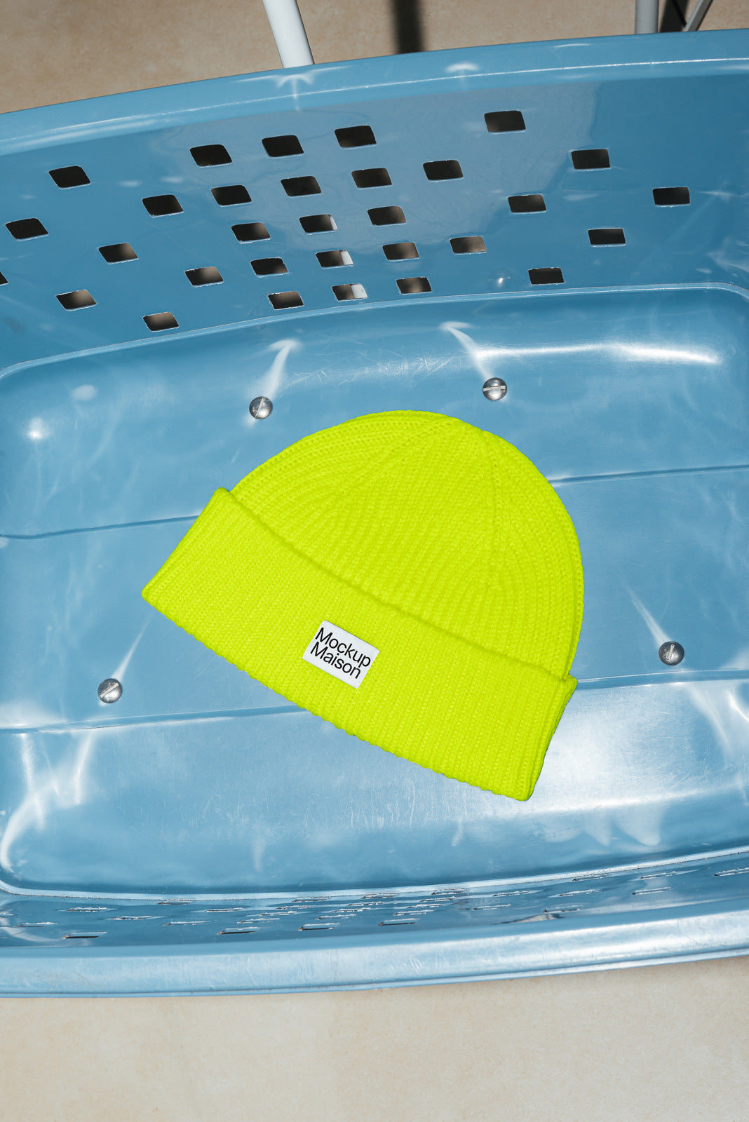PSD mockup of a bright yellow beanie with a label resting in a blue perforated basket.