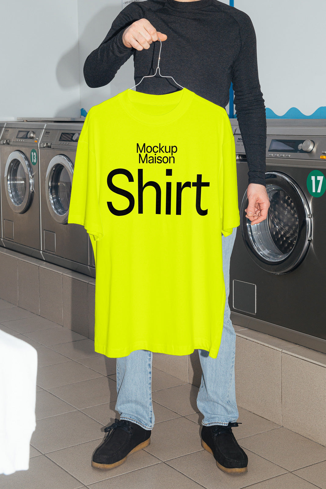 PSD mockup of a person holding a neon yellow T-shirt on a hanger in a laundromat, with the text "Mockup Maison Shirt" printed on it.