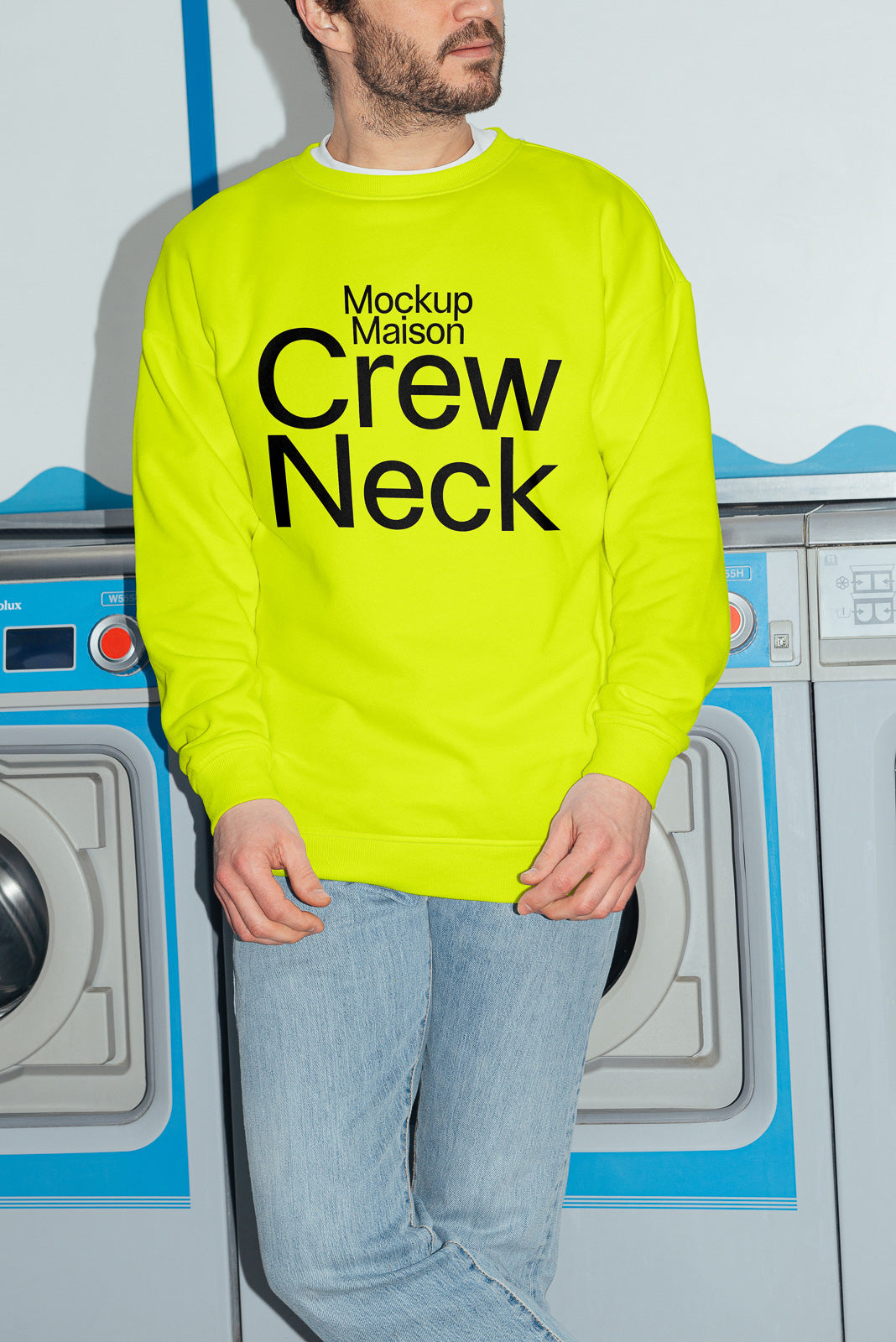PSD mockup of a person in a bright yellow crew neck sweatshirt with bold black text, standing in front of washing machines, wearing jeans.