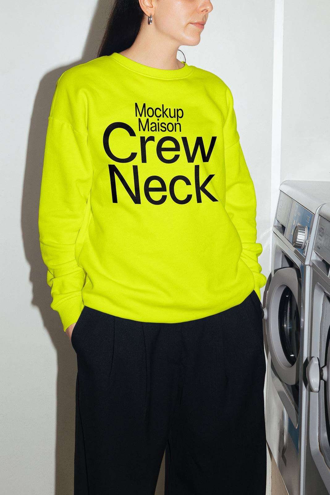PSD mockup of a bright yellow crew neck sweatshirt with bold text, modeled indoors next to a washing machine, highlighting apparel design.
