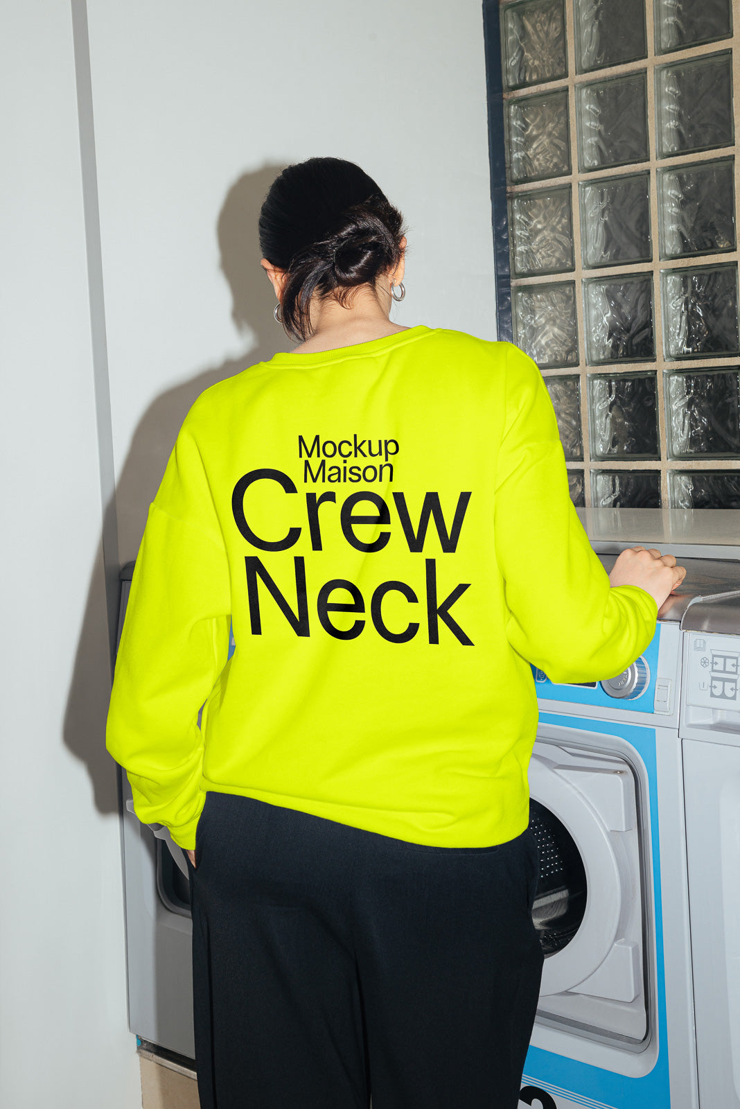 PSD mockup of a person wearing a bright yellow crew neck sweatshirt with text "Mockup Maison Crew Neck" standing near a washer in a laundry room.