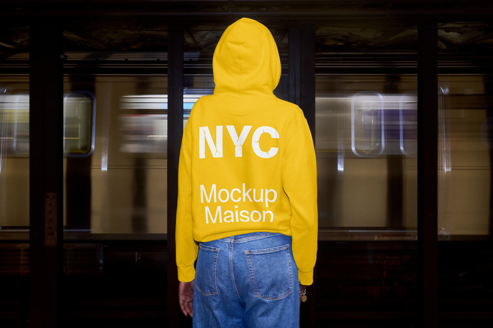 PSD mockup of a person wearing a yellow hoodie with "NYC Mockup Maison" text, standing in front of a moving subway train.