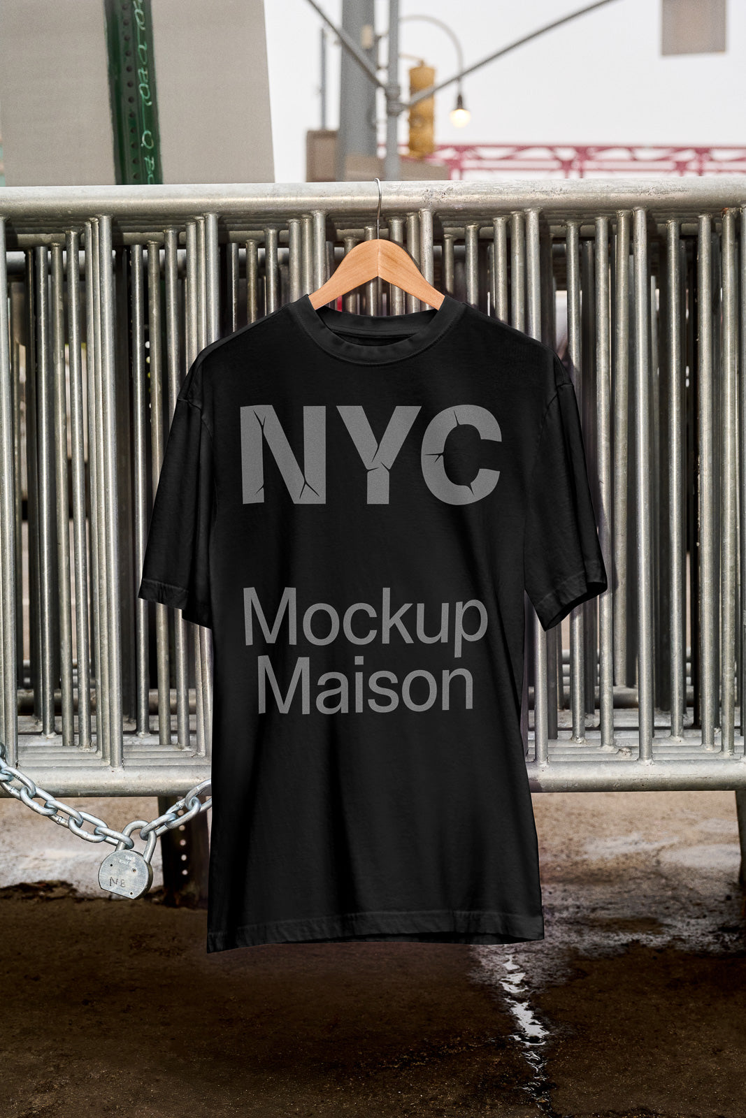 PSD mockup of a black T-shirt hanging on a wooden hanger against metal bars. The shirt features "NYC Mockup Maison" in bold letters.