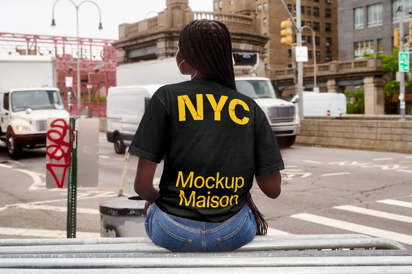 PSD mockup of a person seated on a railing in an urban setting wearing a black T-shirt with "NYC Mockup Maison" in yellow text.