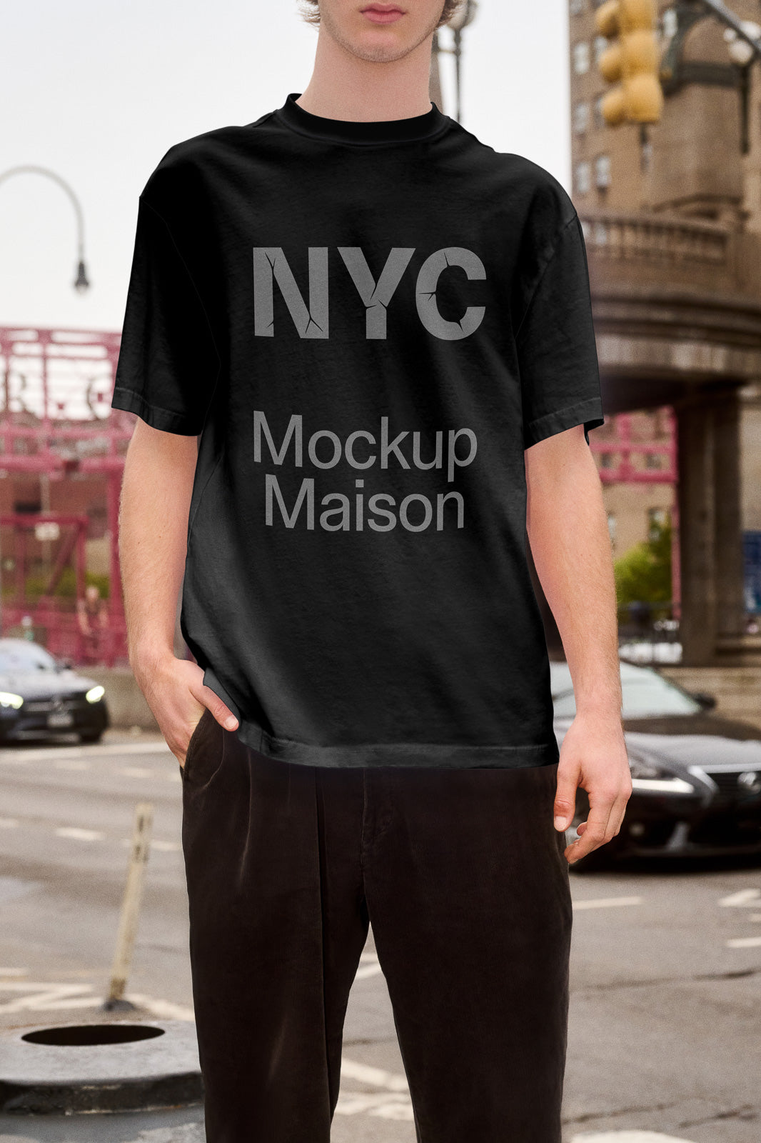 PSD mockup of a black T-shirt featuring "NYC Mockup Maison" text, worn by a person standing on a street with urban architecture.