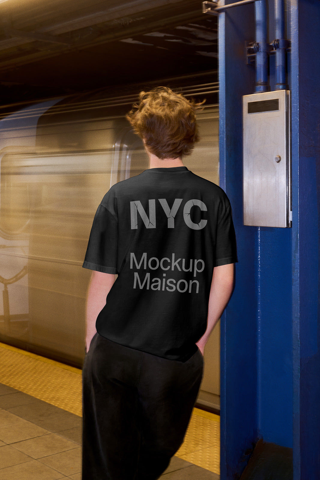 PSD mockup of person wearing a black T-shirt with "NYC Mockup Maison" text, standing on a subway platform with a train in motion.