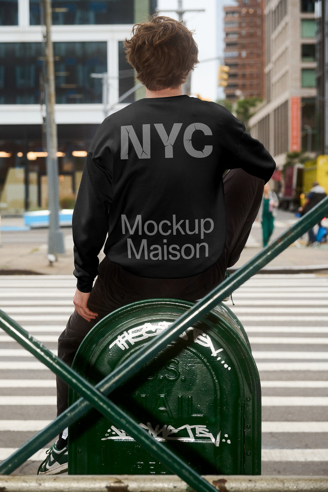 PSD mockup of a person sitting on a mail box in an urban setting, wearing a black sweater with "NYC Mockup Maison" printed on the back.