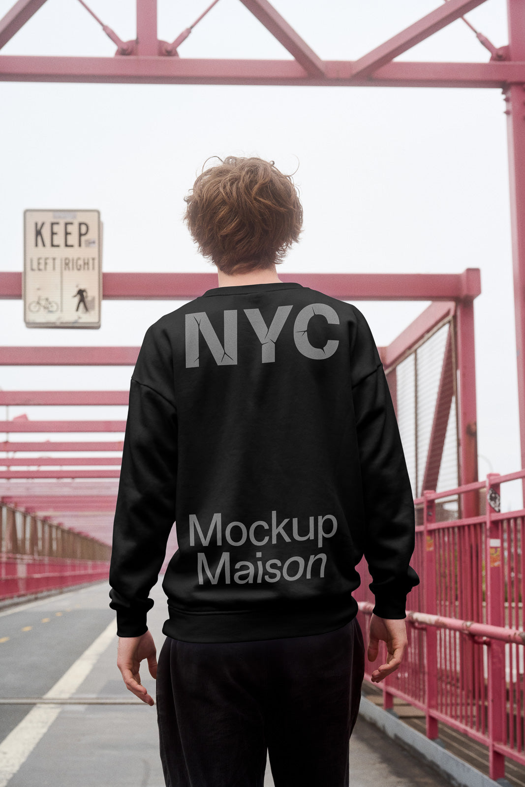 PSD mockup of a person wearing a black sweatshirt with "NYC" text, standing on a bridge with pink railings and directional signage.