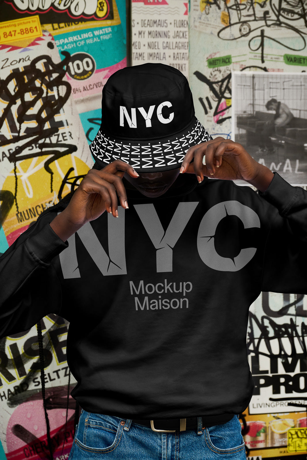 PSD mockup of a person wearing a black NYC bucket hat and matching sweatshirt with graffiti-covered wall background, emphasizing urban fashion style.